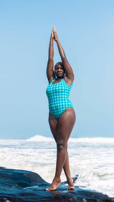 Confident woman in swimsuit posing by ocean waves on a sunny day in Lagos.