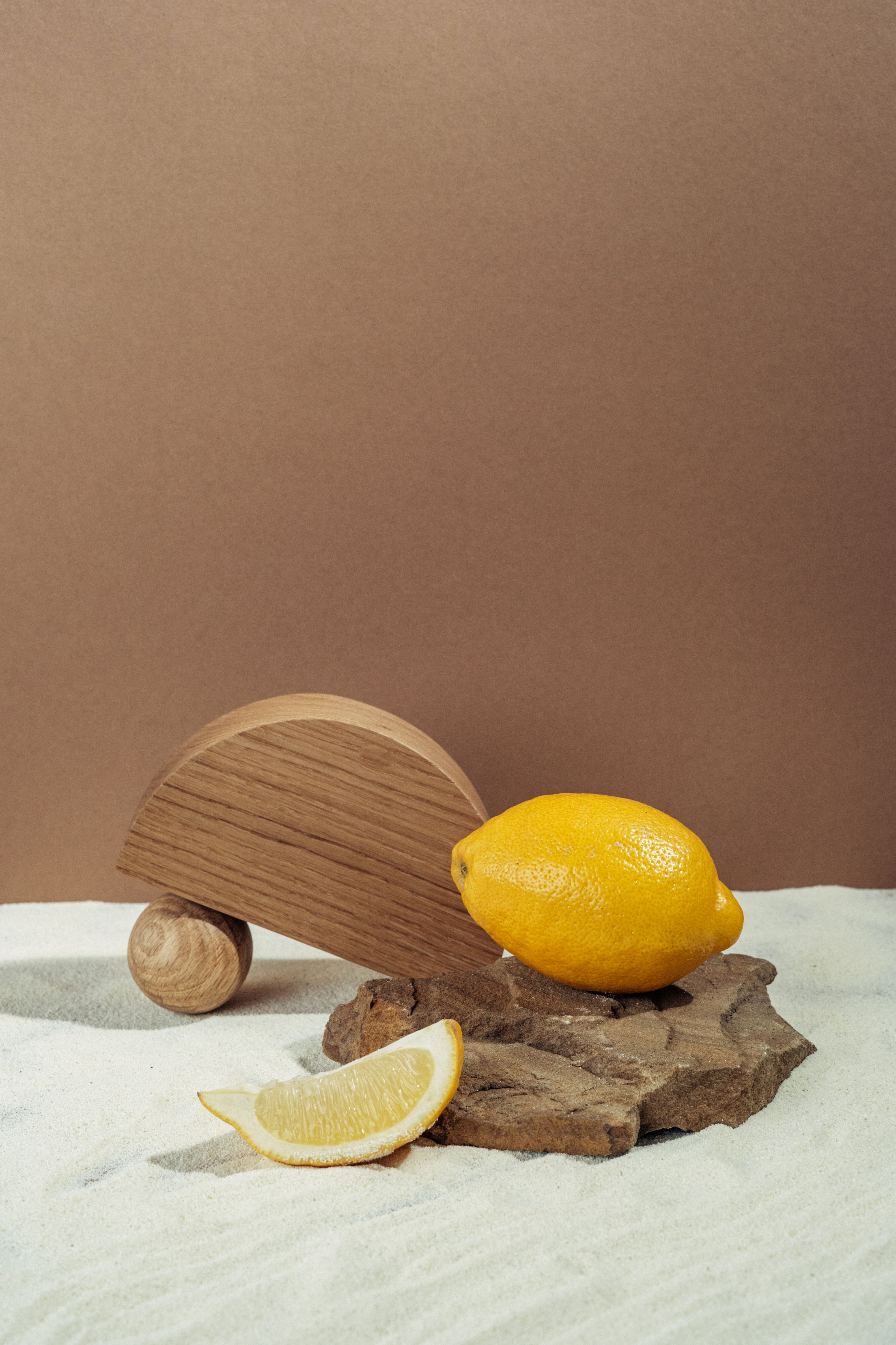 A fresh lemon placed on a wooden toy against a minimalist backdrop, ideal for food or product photography.