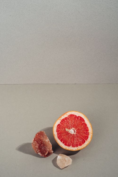 Free A fresh slice of grapefruit next to rock sugar on a minimalist gray surface. Stock Photo