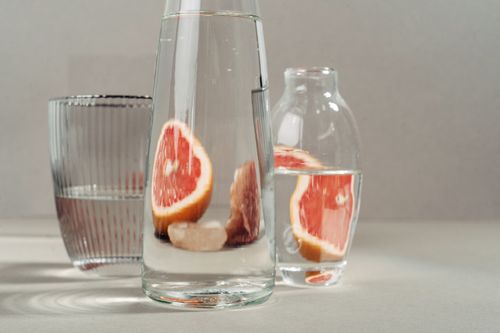 Free Modern still life of grapefruit slices in water-filled glass bottles on neutral background. Stock Photo