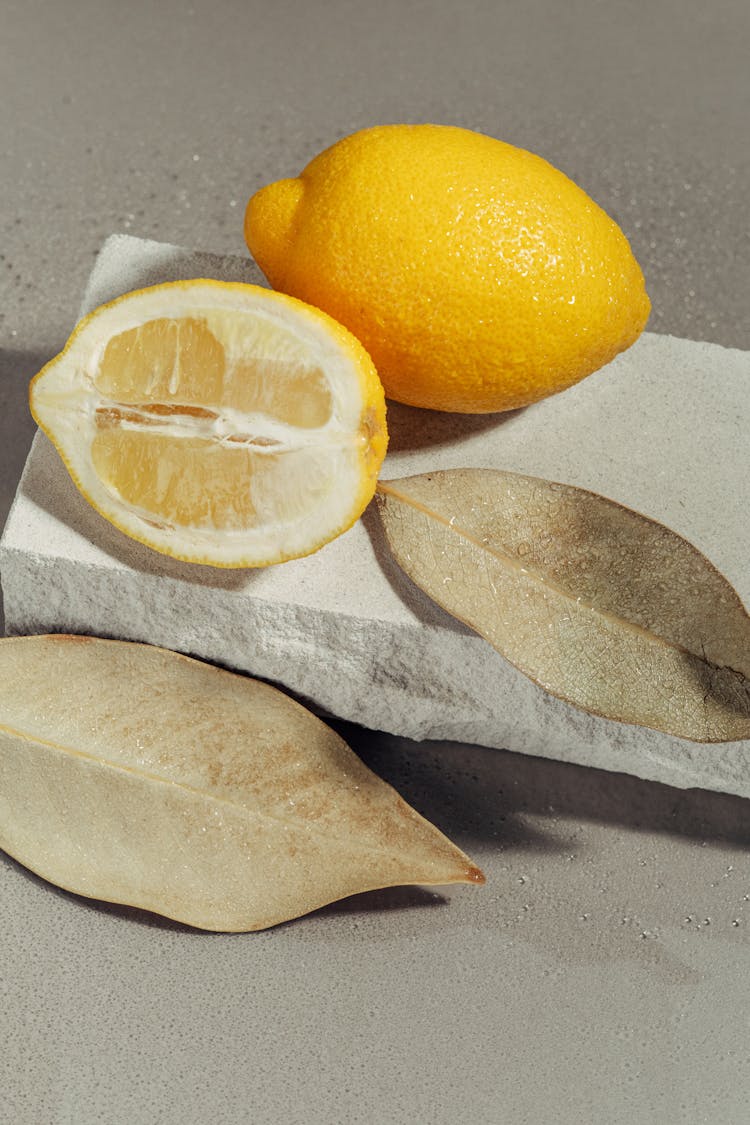 Whole And Sliced Lemon On Stone Beside Dry Leaves