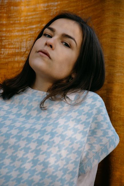 Portrait of a young woman wearing a blue houndstooth sweater posing confidently against a textured background.