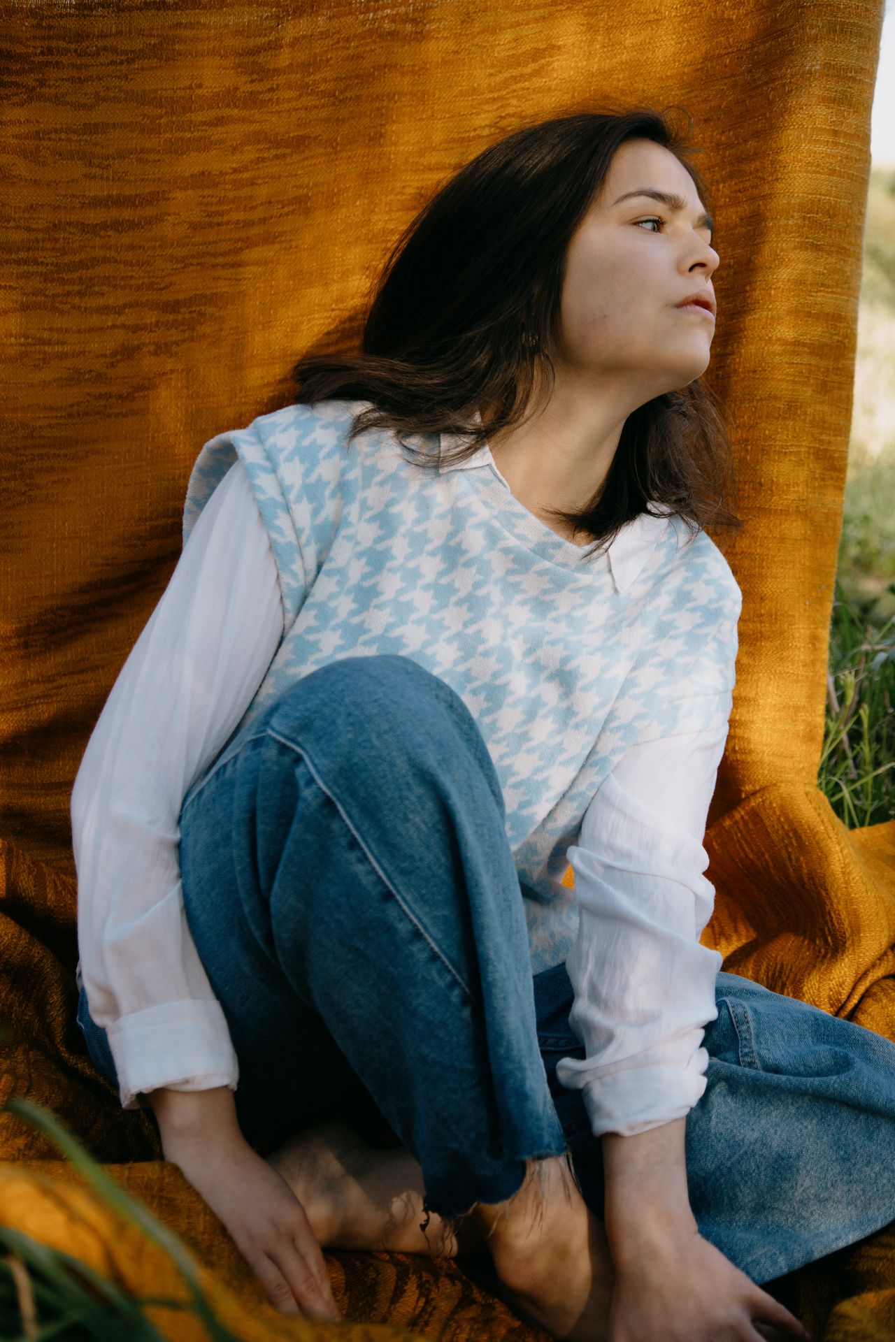 Woman layering a blue and white houndstooth check knit vest over a white collared shirt with jeans