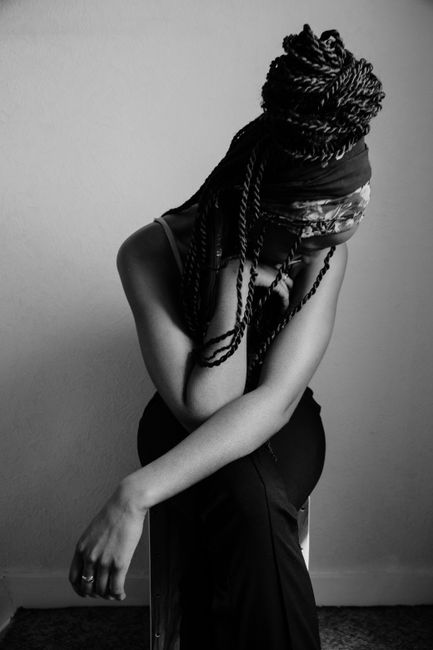 Artistic black and white portrait of a woman sitting with braided hair, exuding a moody fashion vibe.