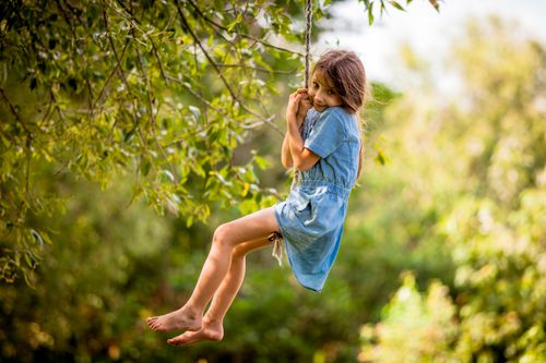 Free A happy young girl enjoying a playful moment on a rope swing in a sunny outdoor setting. Stock Photo