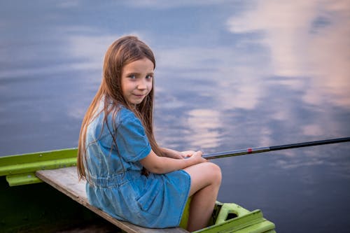 Free Woman in Blue Dress Sitting on Brown Wooden Boat Stock Photo