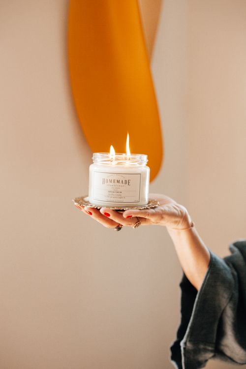 Free A hand holding a lit homemade candle against a blurred background indoors. Stock Photo