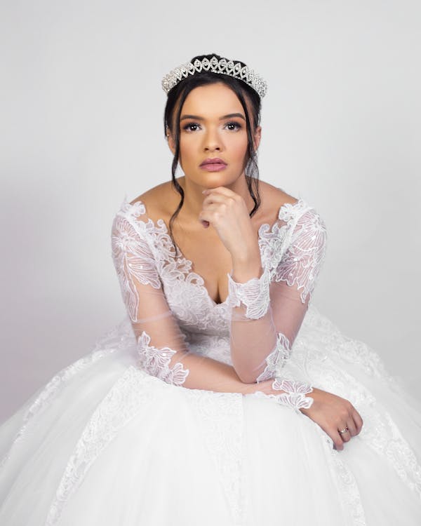 Elegant young woman in wedding dress sitting in white studio and looking at camera