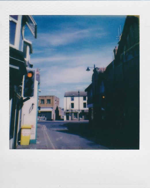 Polaroid style photo of a small town street with classic buildings and a clear blue sky.