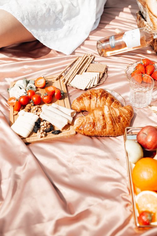 Free Luxurious outdoor picnic with croissants, cheese, fruits, and wine on satin fabric. Stock Photo