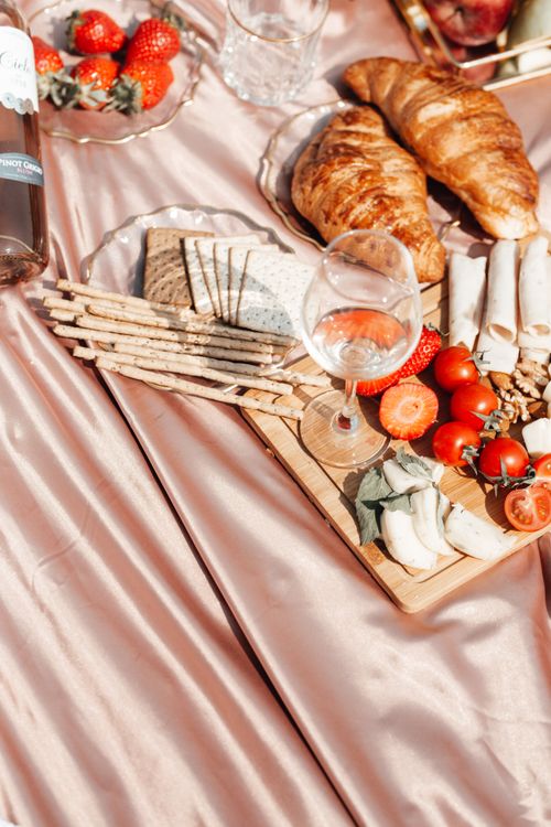 Free Luxurious picnic setup featuring croissants, wine, and fresh produce on a satin blanket. Stock Photo