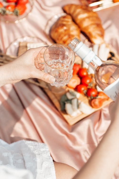 Free A close-up of a woman's hand pouring wine during a picnic with croissants and fresh fruits. Stock Photo