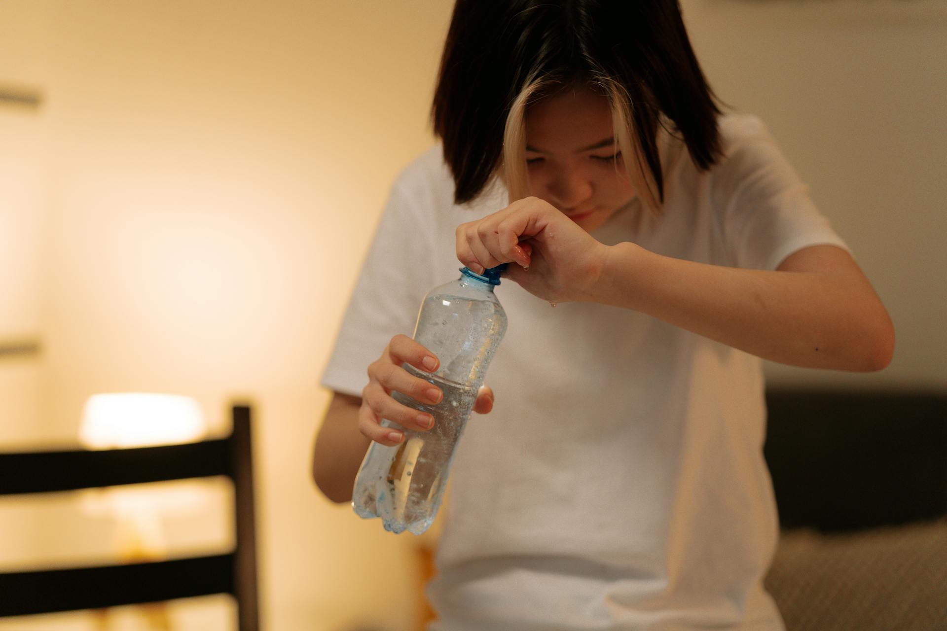 A young woman attempts to open a plastic water bottle at home.