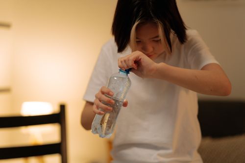 Free A young woman attempts to open a plastic water bottle at home. Stock Photo