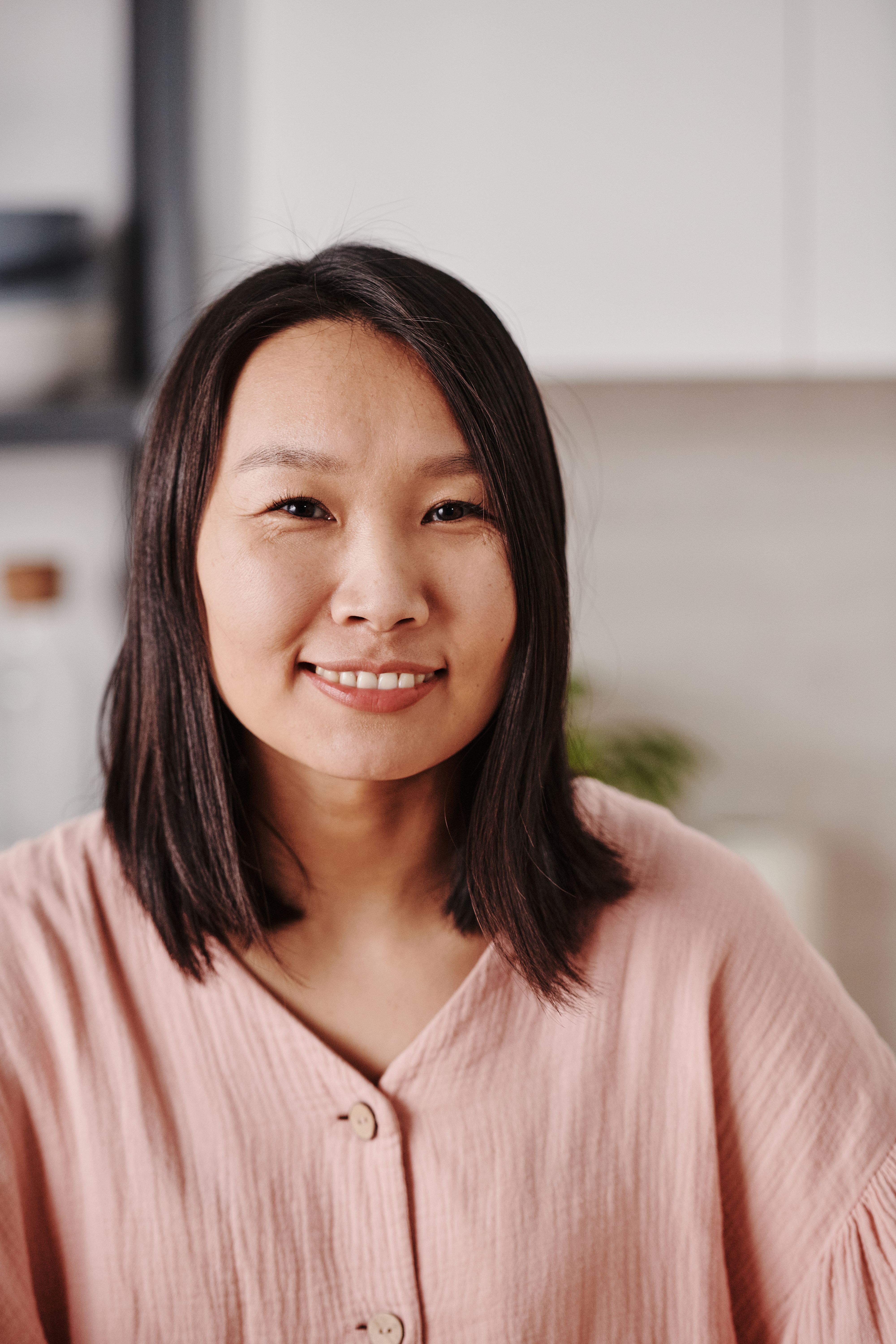 Portrait of a smiling woman in a pink blouse, posing indoors with a neutral background.