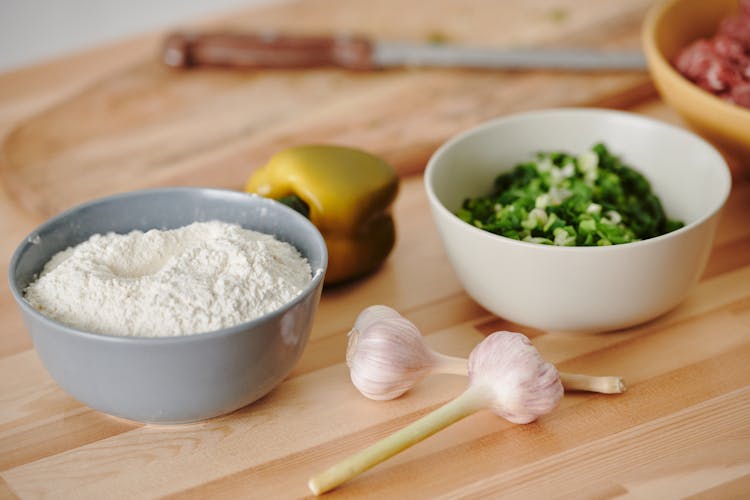 A Bowl Of White Flour Near A Bowl Of Chopped Scallions