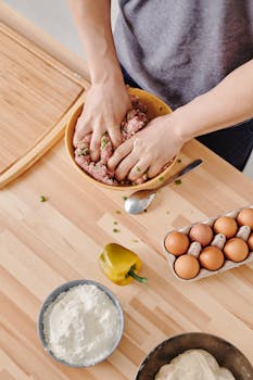 A person prepares a meal by mixing minced meat and ingredients on a wooden counter.