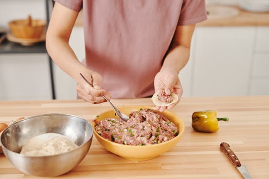 Person preparing dumplings with meat and vegetable filling in a kitchen setting.