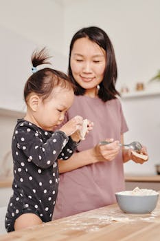 A mother and daughter bonding in the kitchen while making dumplings indoors.