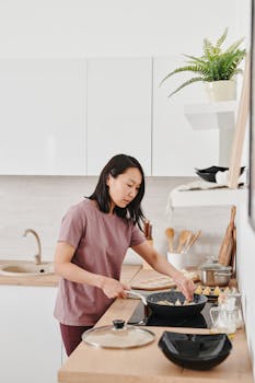 Asian woman preparing dumplings in a modern kitchen setting, demonstrating culinary skills.