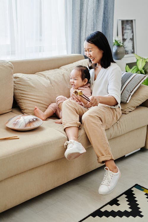 Photo of a Mother and Her Daughter Sitting on a Sofa while Smiling