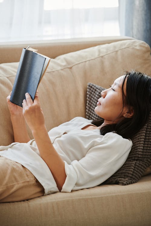 A Woman Reading a Book while Lying on a Couch