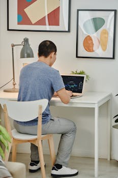 A man in casual attire working remotely on a laptop in a modern home office setting.