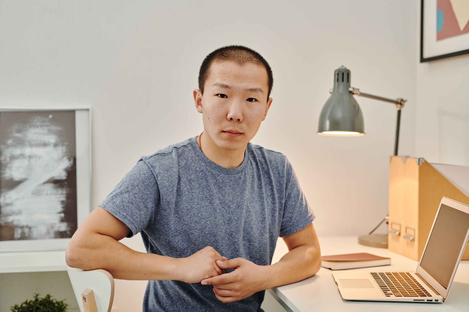 Asian man sitting at a desk with a laptop, engaged in remote work from a stylish home office.