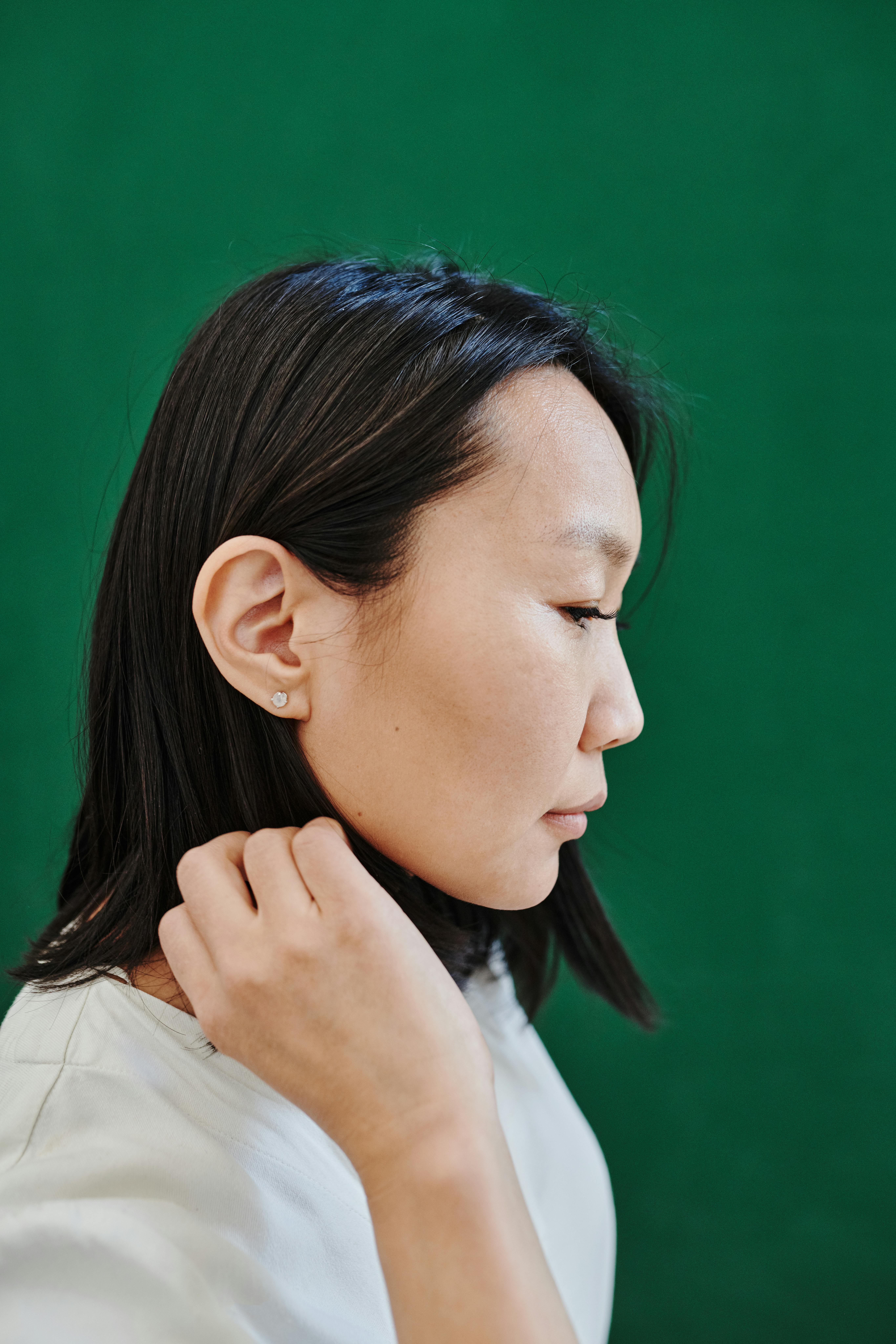 Portrait of an Asian woman in profile against a green backdrop, wearing a white shirt.