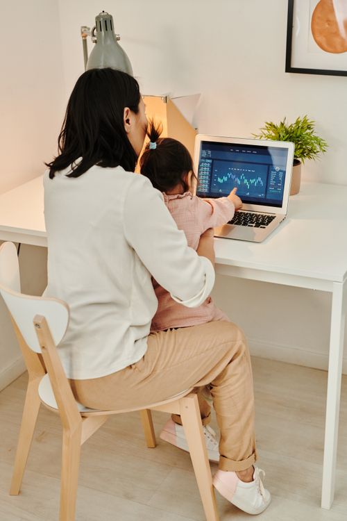 Free Mother working with child on laptop in home office setting, balancing work and family. Stock Photo