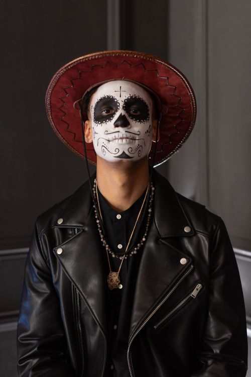 Free Man in face paint, red hat, and leather jacket, capturing a spooky Halloween portrait indoors. Stock Photo