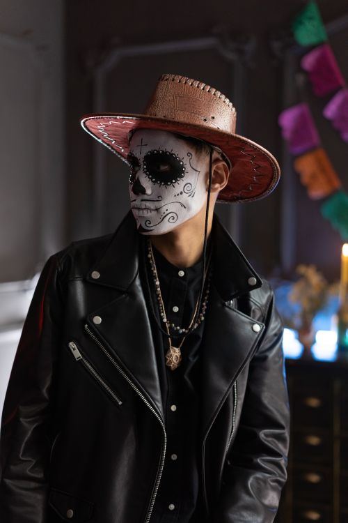 Free Person in leather jacket and sugar skull makeup for Day of the Dead celebration indoors. Stock Photo