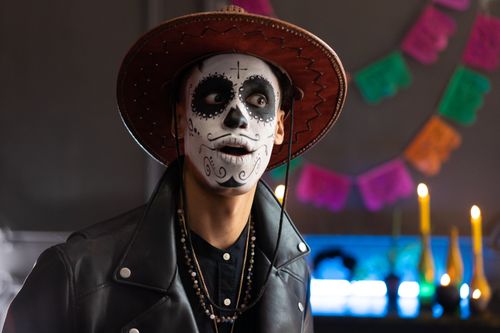 Free Man in Day of the Dead makeup with hat and candles, celebrating tradition indoors. Stock Photo
