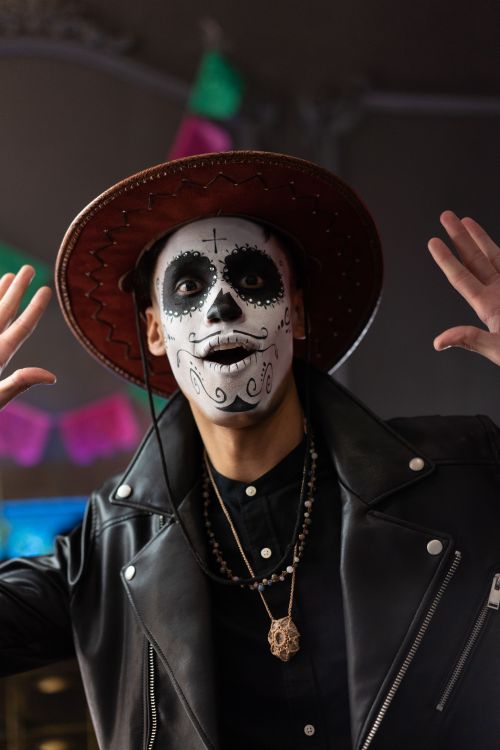 Free Man in skull face paint and leather jacket celebrating Day of the Dead indoors. Stock Photo