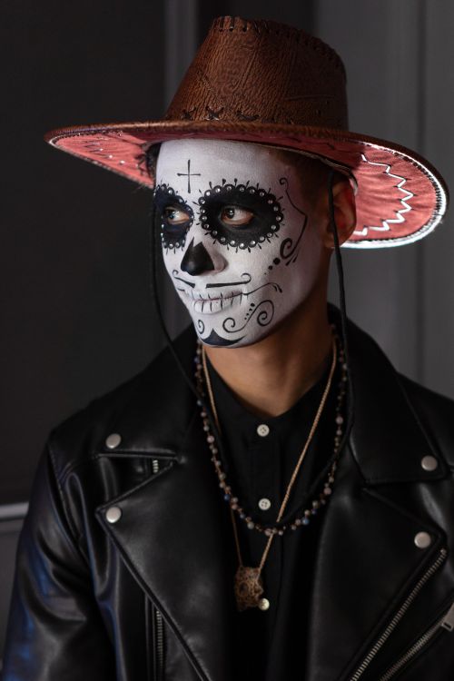 Free Portrait of a man in Dia de los Muertos face paint with a black leather jacket and hat. Stock Photo