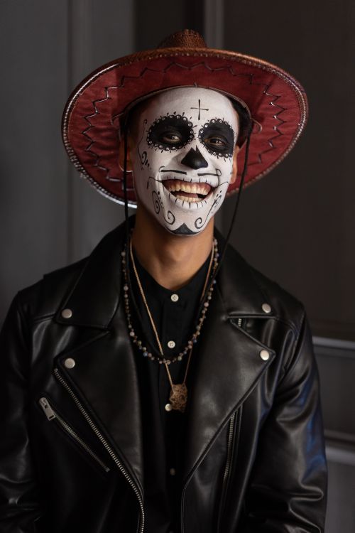 Free A cheerful man wearing Day of the Dead makeup, a cowboy hat, and a leather jacket indoors. Stock Photo