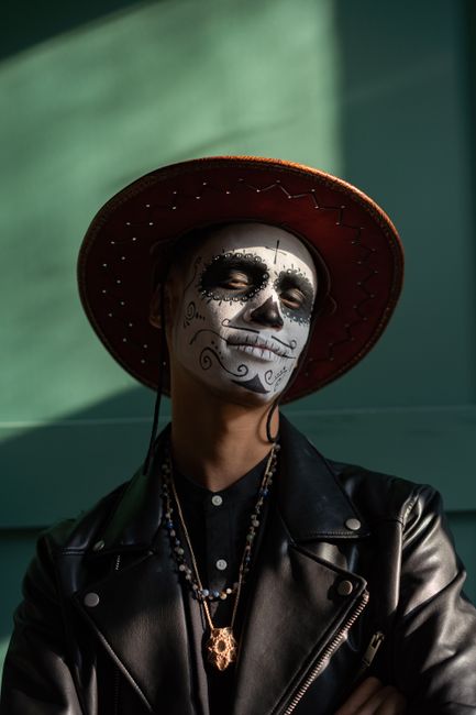 A man in a black leather jacket poses with Dia de los Muertos makeup.