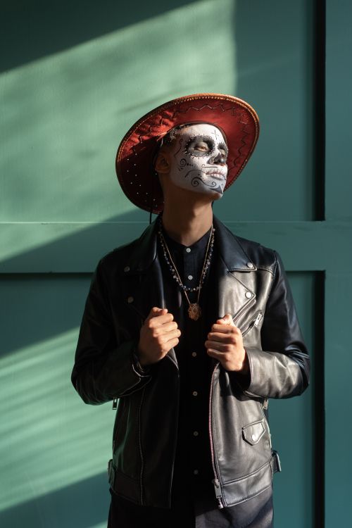 Free Man with painted face and hat posing in a Day of the Dead style indoors with sunlight streaming. Stock Photo