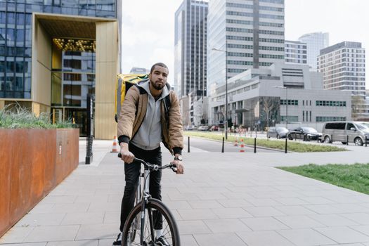 Food courier cycling through urban cityscape with modern skyscrapers.