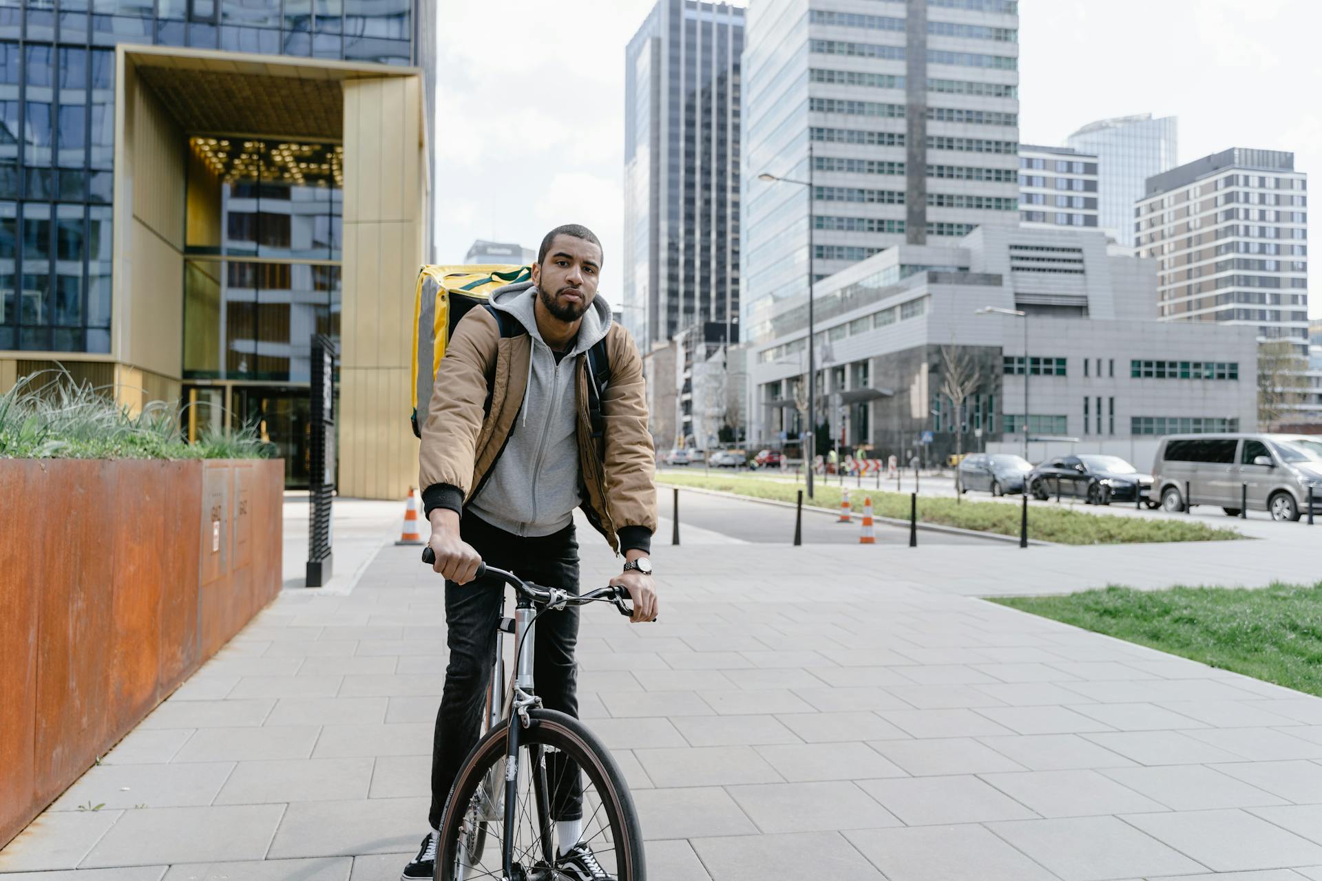 Food courier cycling through urban cityscape with modern skyscrapers.