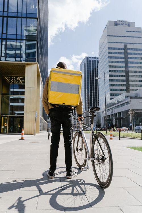Free A courier stands with a bicycle and yellow delivery bag in downtown Warsaw, showcasing urban delivery dynamics. Stock Photo