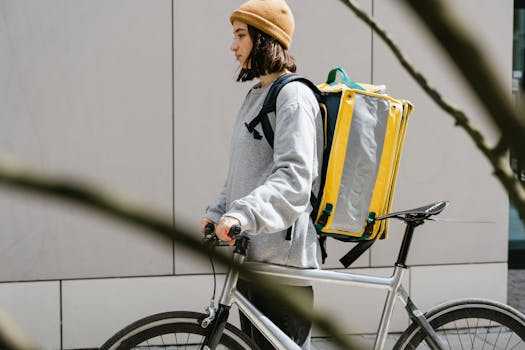 Young courier with a bike and thermal bag on a city street.