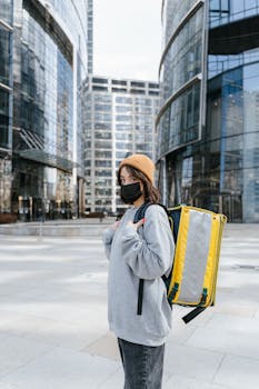 Courier with yellow backpack near glass modern buildings in urban area.