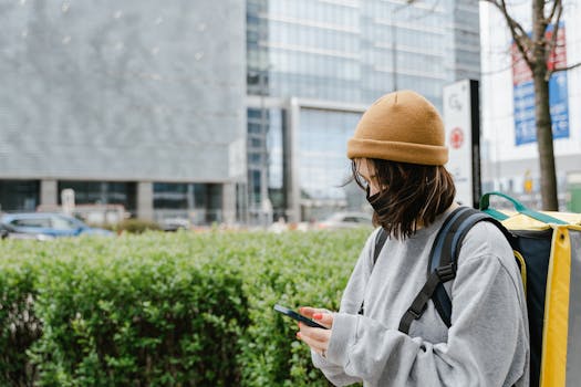Woman with thermal bag checking phone in urban setting, delivering food.