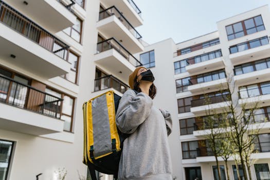 A masked courier carrying a thermal backpack in a modern urban neighborhood.