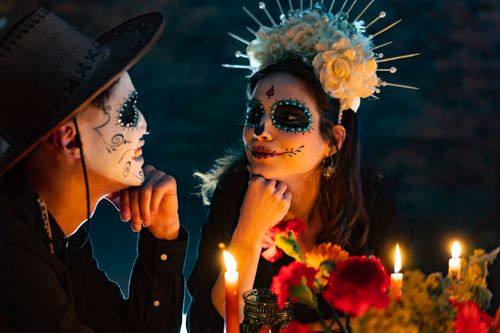 Free Couple in Dia de los Muertos style makeup celebrating with candles and flowers. Stock Photo