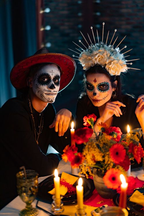 Free Vibrant Day of the Dead celebration featuring traditional makeup and costumes at a candlelit dinner. Stock Photo