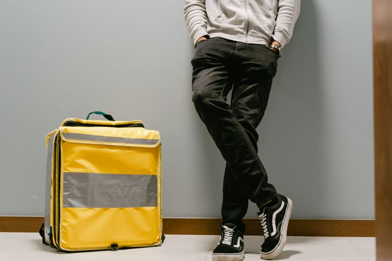 A courier resting against a wall with a yellow thermal delivery bag — photo by MART PRODUCTION on Pexels
