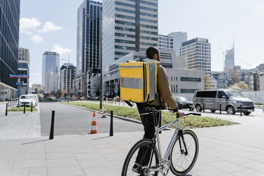 Cyclist with a large yellow thermal bag biking through a modern city downtown area.