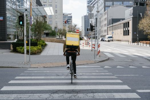 Cyclist with thermal bag crossing street in downtown Warsaw, Poland.